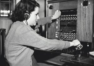 Eine weibliche Telefonistin in den 1940er Jahren, die ein Headset trägt und eine Telefonschalttafel bedient.